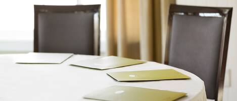 A round table with a white tablecloth, three laptops, and two dark chairs.