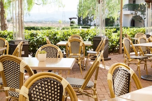 An outdoor seating area with wicker chairs and tables, surrounded by greenery and a view of the landscape.