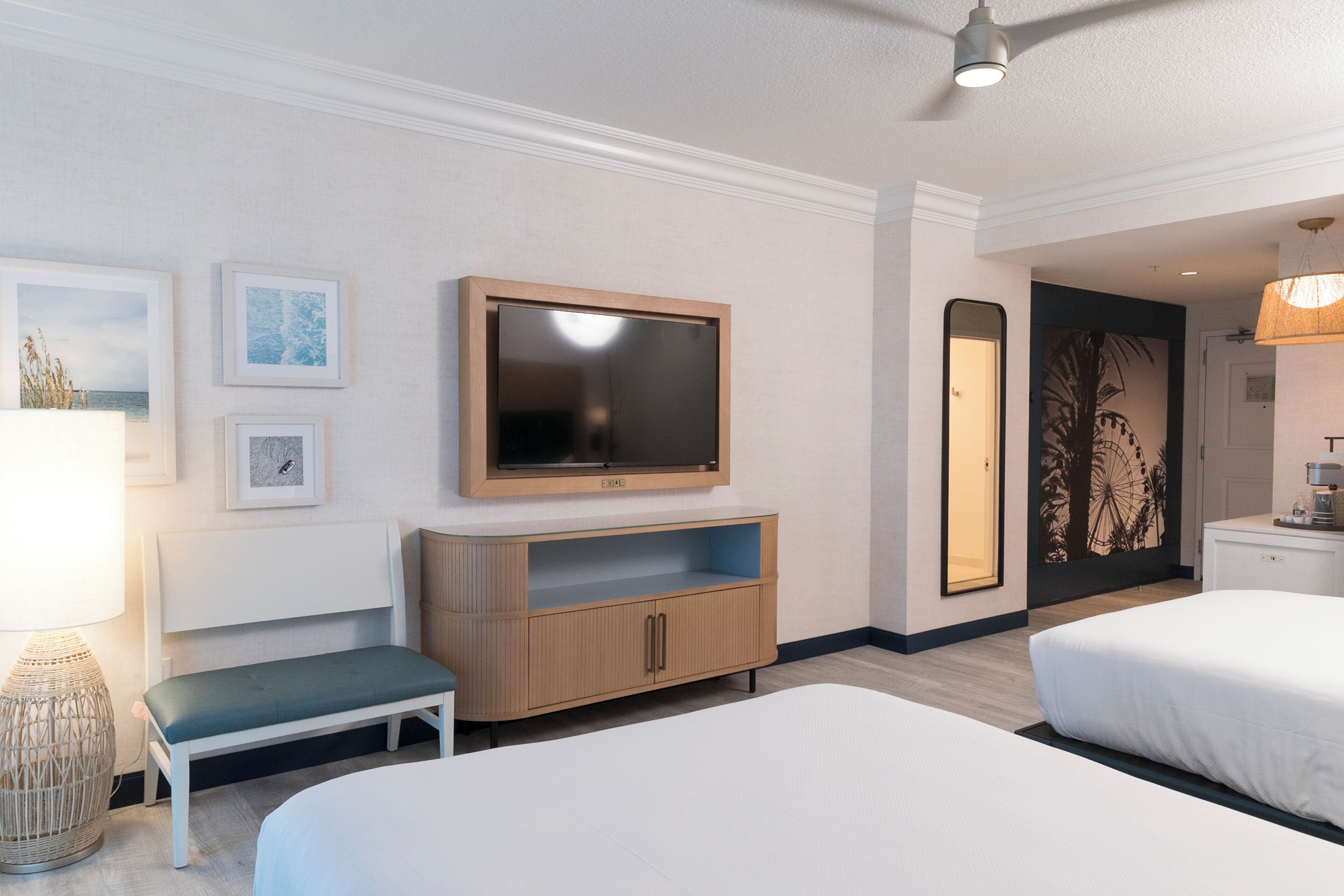 Une chambre d’hôtel avec deux lits, un téléviseur, un banc et un téléviseur fixé au mur.
