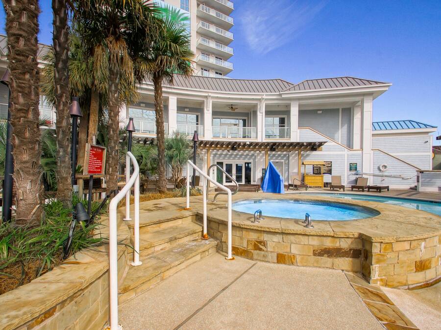 A pool area with a hot tub, palm trees, and a building with balconies.