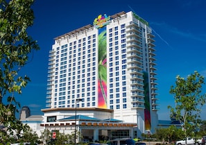 Un hotel alto con un mural colorido en la fachada, varios balcones y un cielo azul despejado al fondo.