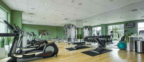 Un gimnasio con máquinas de cardio, bancos de pesas y espejos en las paredes.
