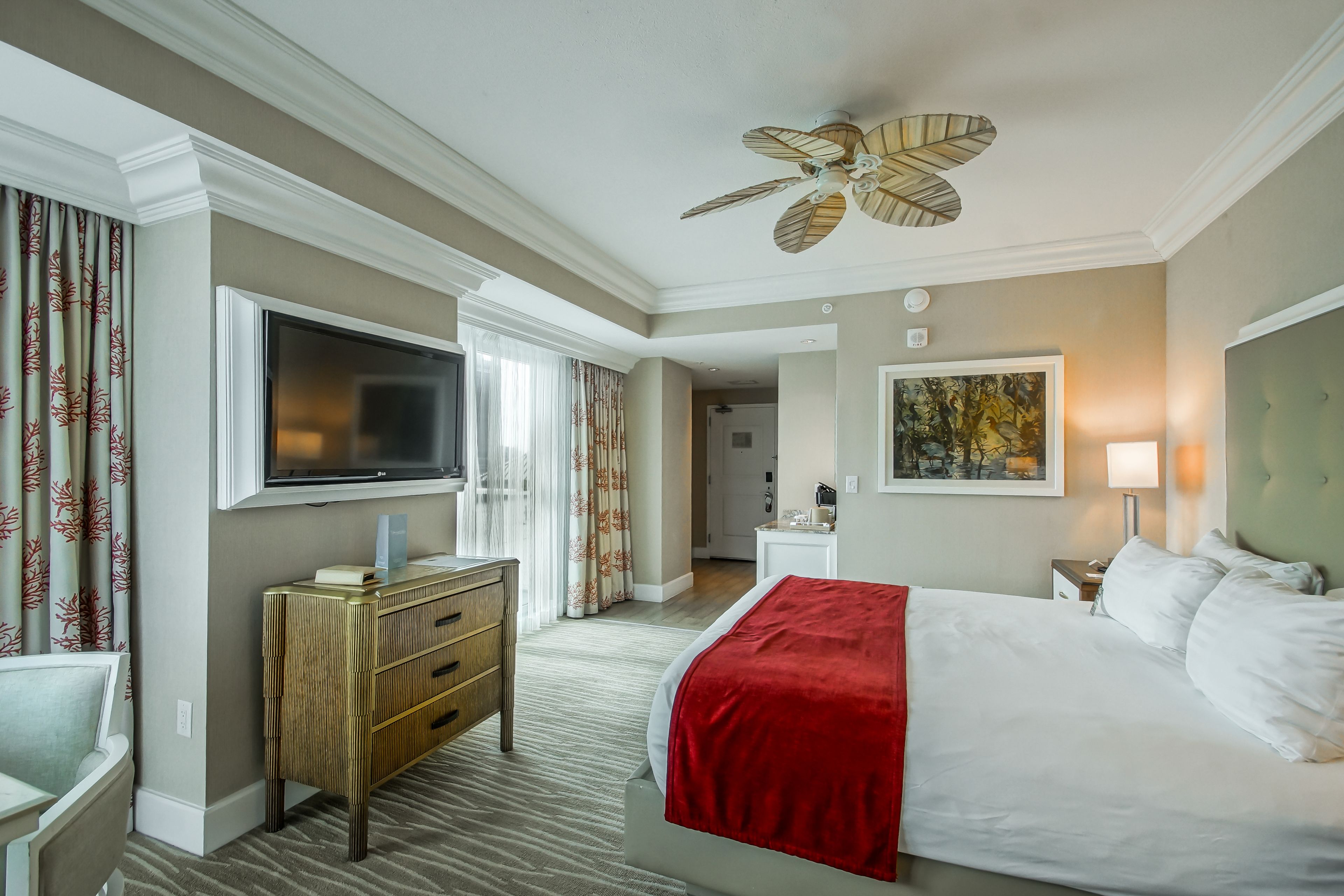 A hotel room with a bed, a television, a dresser, and a ceiling fan.