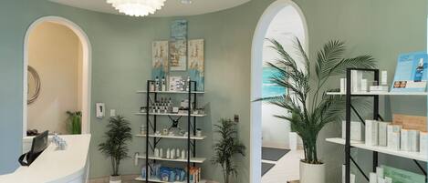 A reception area with a white reception desk, shelves with products, and potted plants.