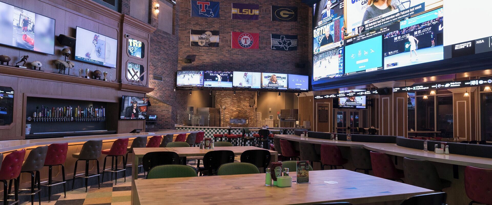 A sports bar with multiple screens displaying various sports events, a bar area with a selection of bottles, and seating arrangements for patrons.