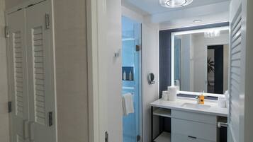 Un baño moderno con cabina de ducha de vidrio, un tocador blanco con un espejo grande, y una toalla colgada en la puerta.
