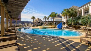 A pool area with lounge chairs, a thatched-roof structure, and palm trees. - Margaritaville Resort Casino (Bossier City)