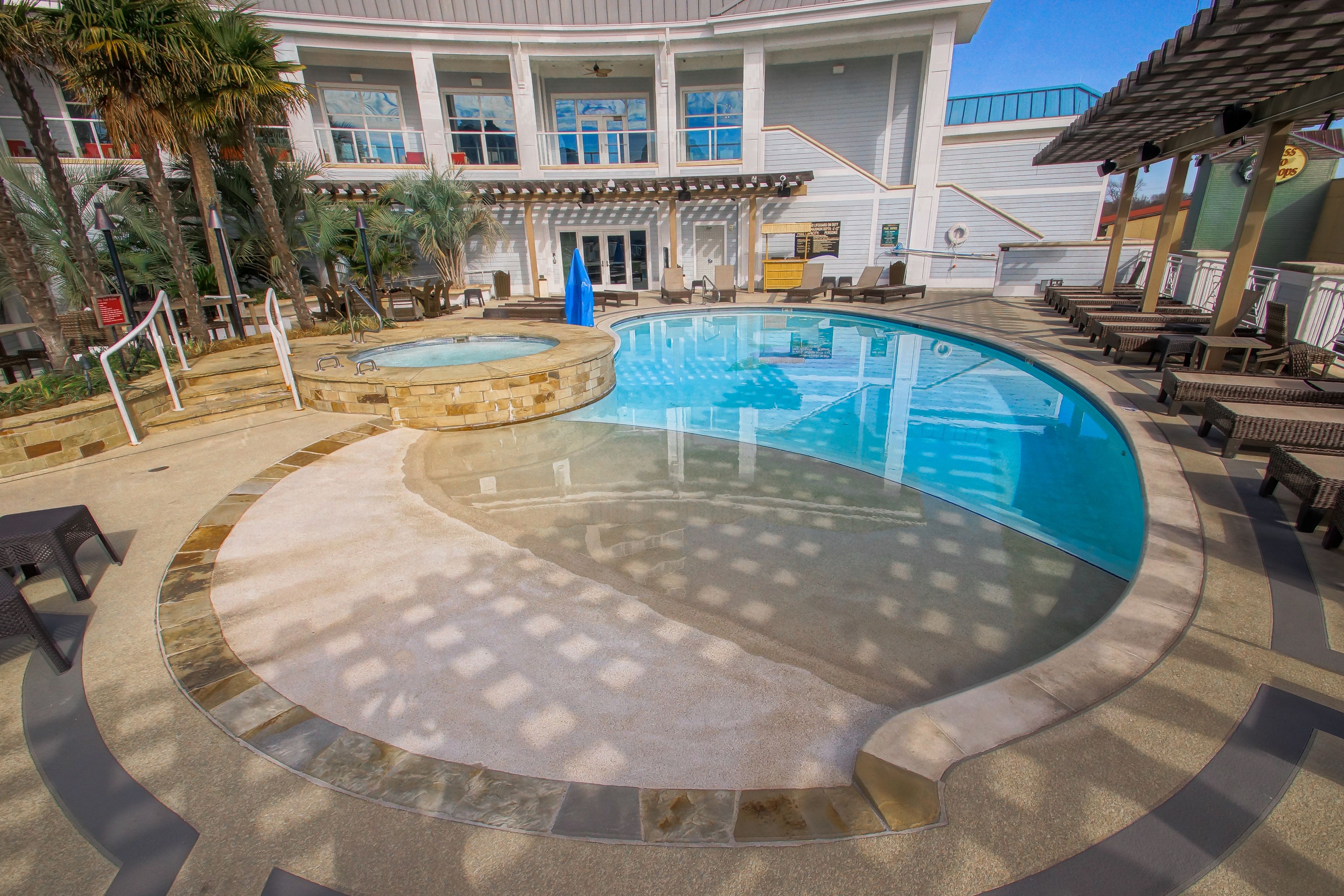 A pool area with a hot tub, lounge chairs, and a building in the background.