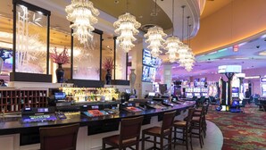 A bar area with multiple bar stools, a counter with a cash register, and a large screen displaying content. - Margaritaville Resort Casino (Bossier City)