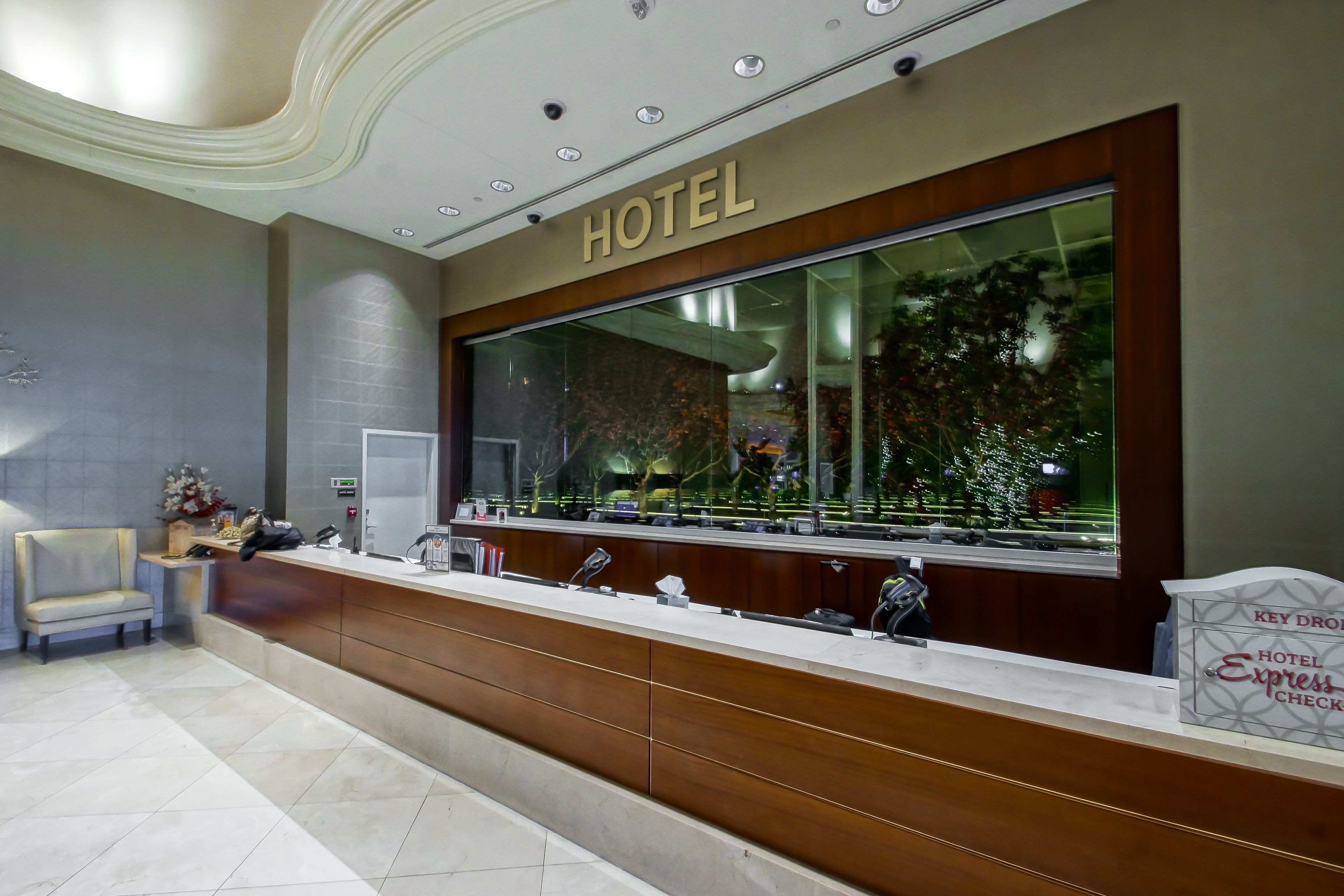 Zona de recepción de un hotel con un ventanal grande, un mostrador de recepción, un área de descanso y un cartel que indica servicio de entrega de llaves.