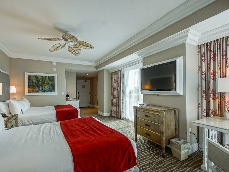 A hotel room with two beds, a TV, a desk, and a ceiling fan.