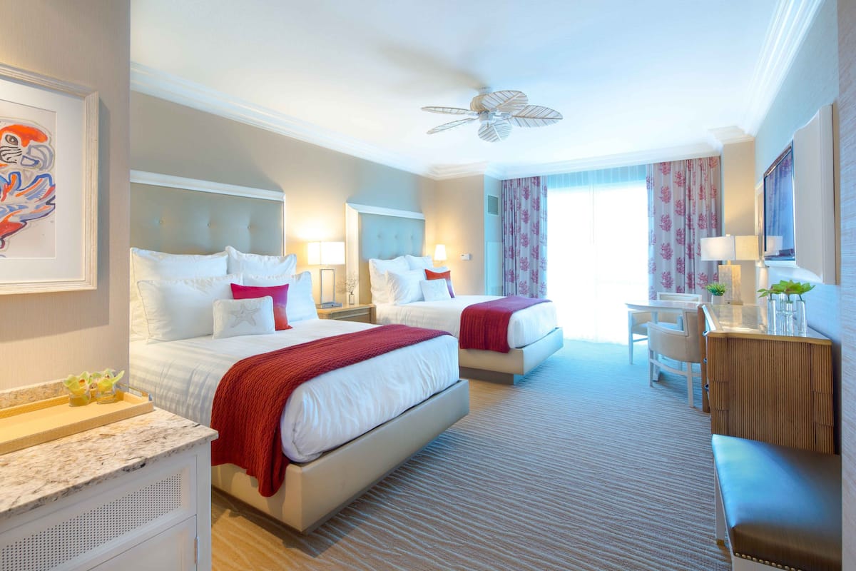 A hotel room with two beds, a desk, a chair, and a ceiling fan.
