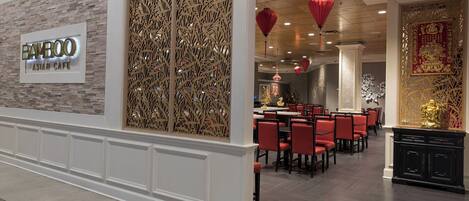 Interior de un restaurante con un letrero que dice 'Bamboo Asian Cafe', sillas rojas y decoración tradicional.