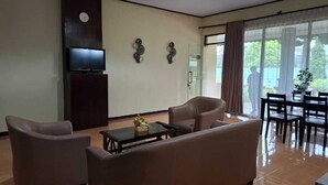 Ein Wohnzimmer mit einer Couch, Sesseln, einem Couchtisch, einem Fernseher und einem Essbereich mit Tisch und Stühlen.