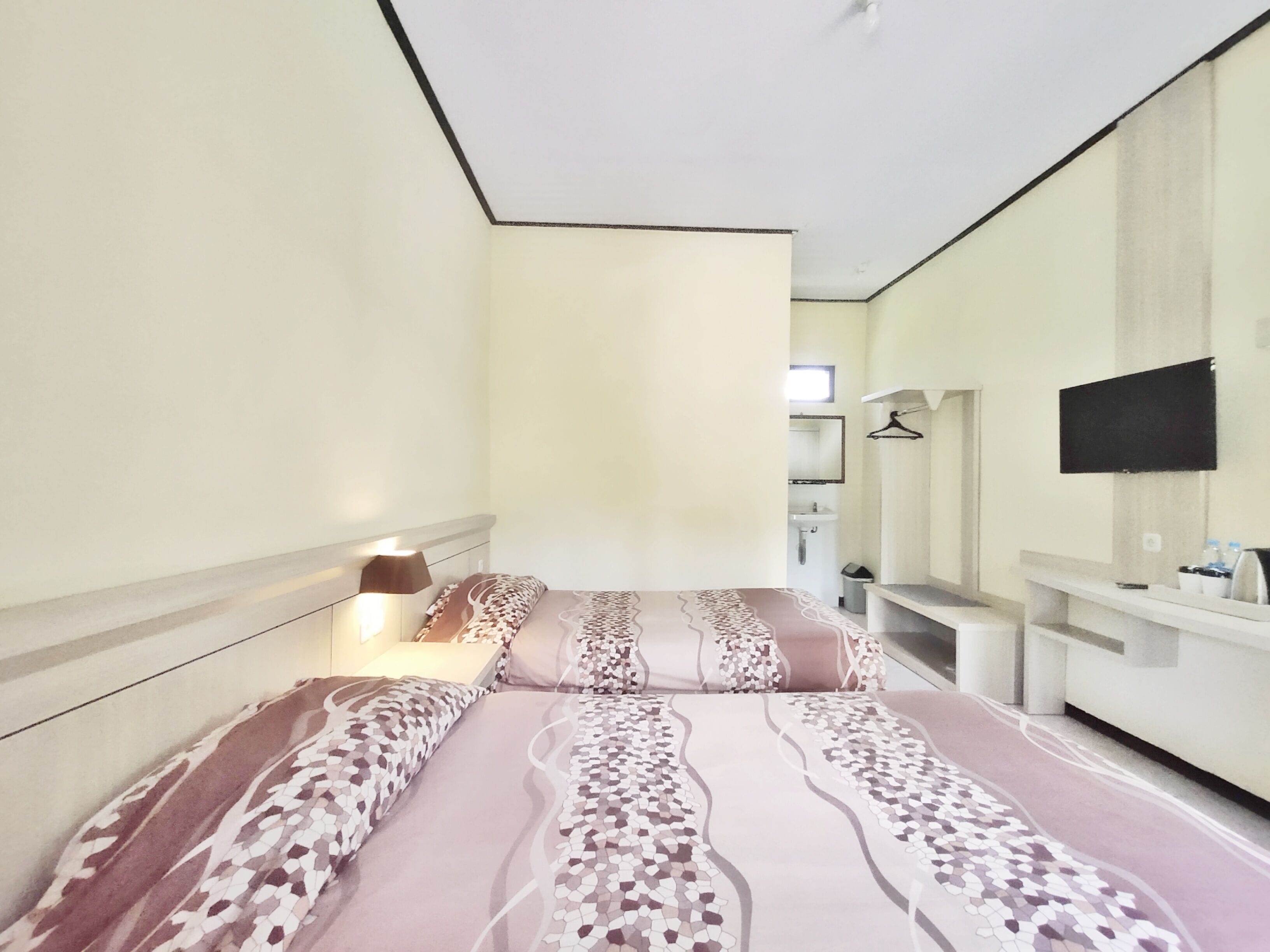 Een hotelkamer met een bed, een bedlampje, een aan de muur bevestigde televisie en een klein badgedeelte zichtbaar op de achtergrond.