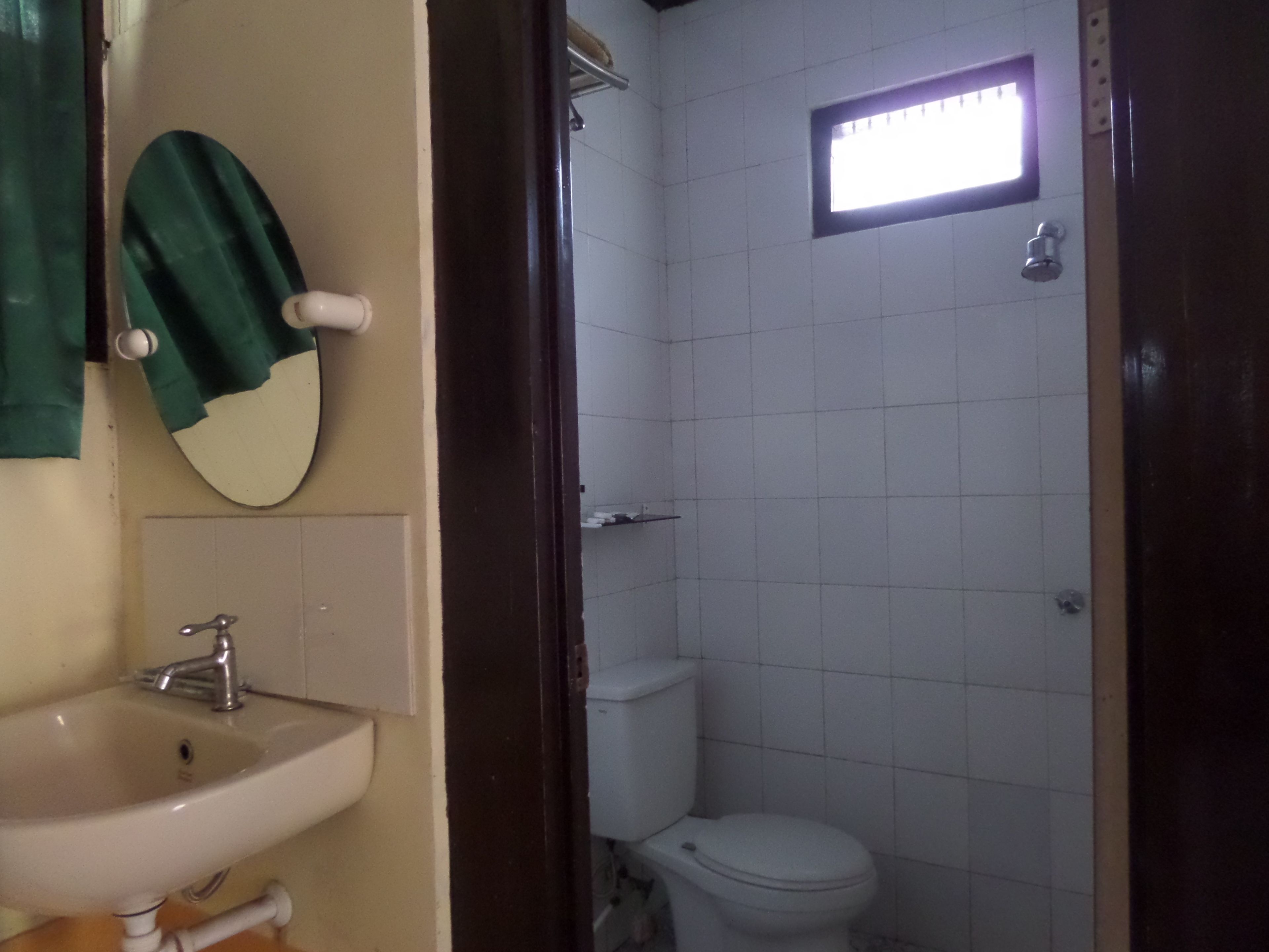 A bathroom with a sink, mirror, toilet, and a small window.