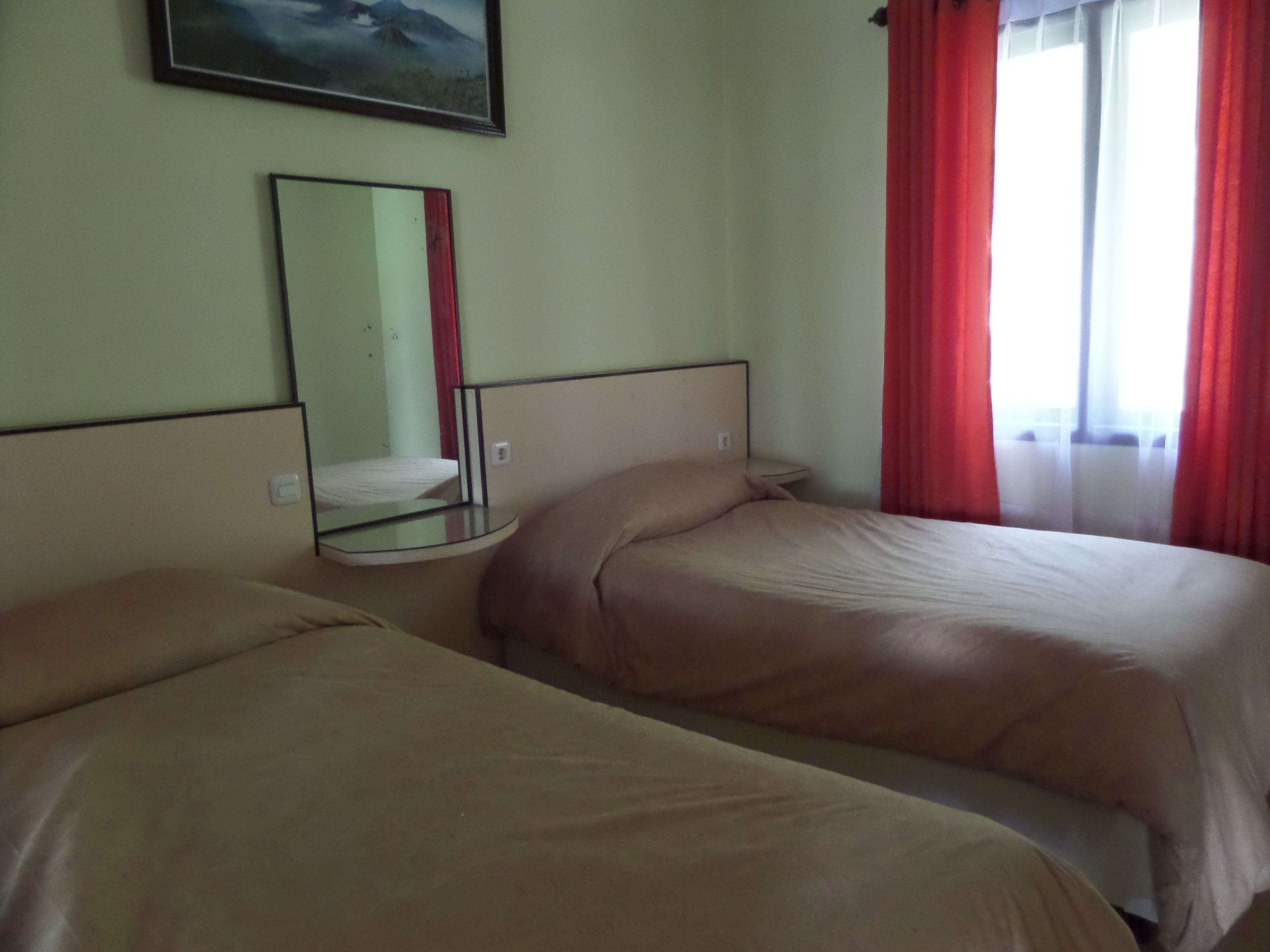 Une chambre d’hôtel avec deux lits, une table de chevet, un miroir et une fenêtre avec des rideaux rouges.