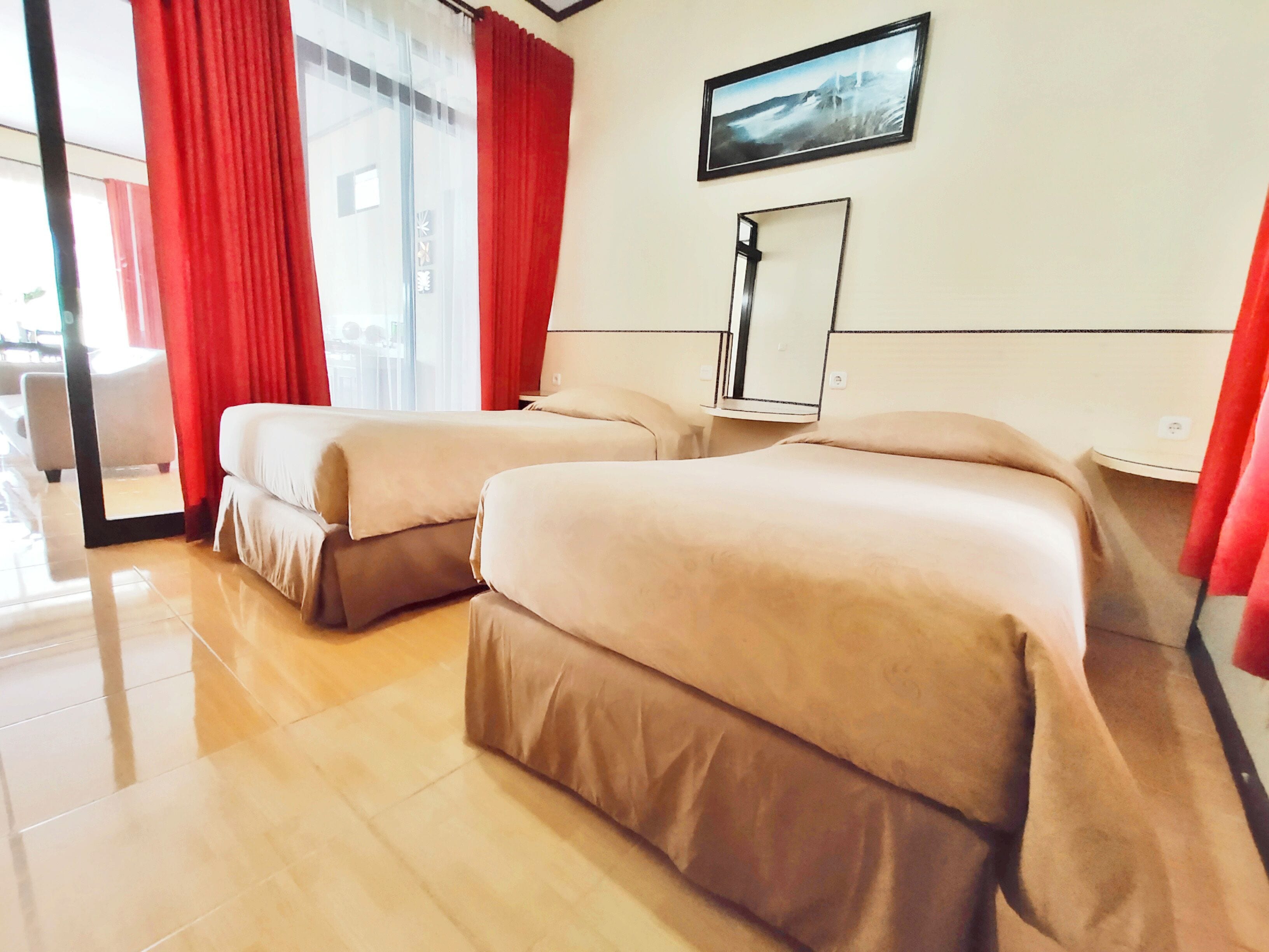 A hotel room with two beds, a large window with red curtains, a flat-screen TV, and a mirror on the wall.