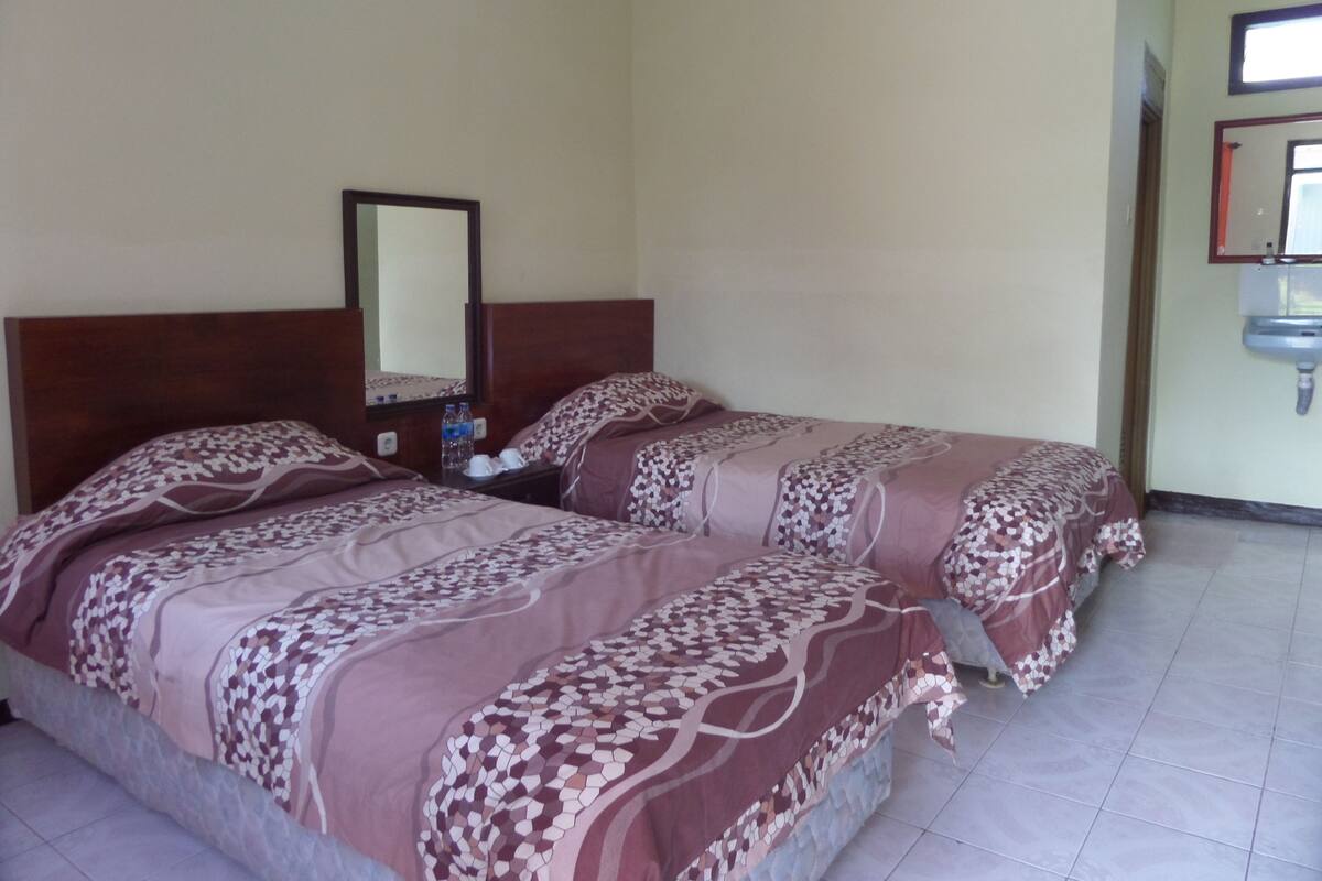 Quarto de hotel com duas camas, uma mesa de cabeceira, um espelho e uma pia.
