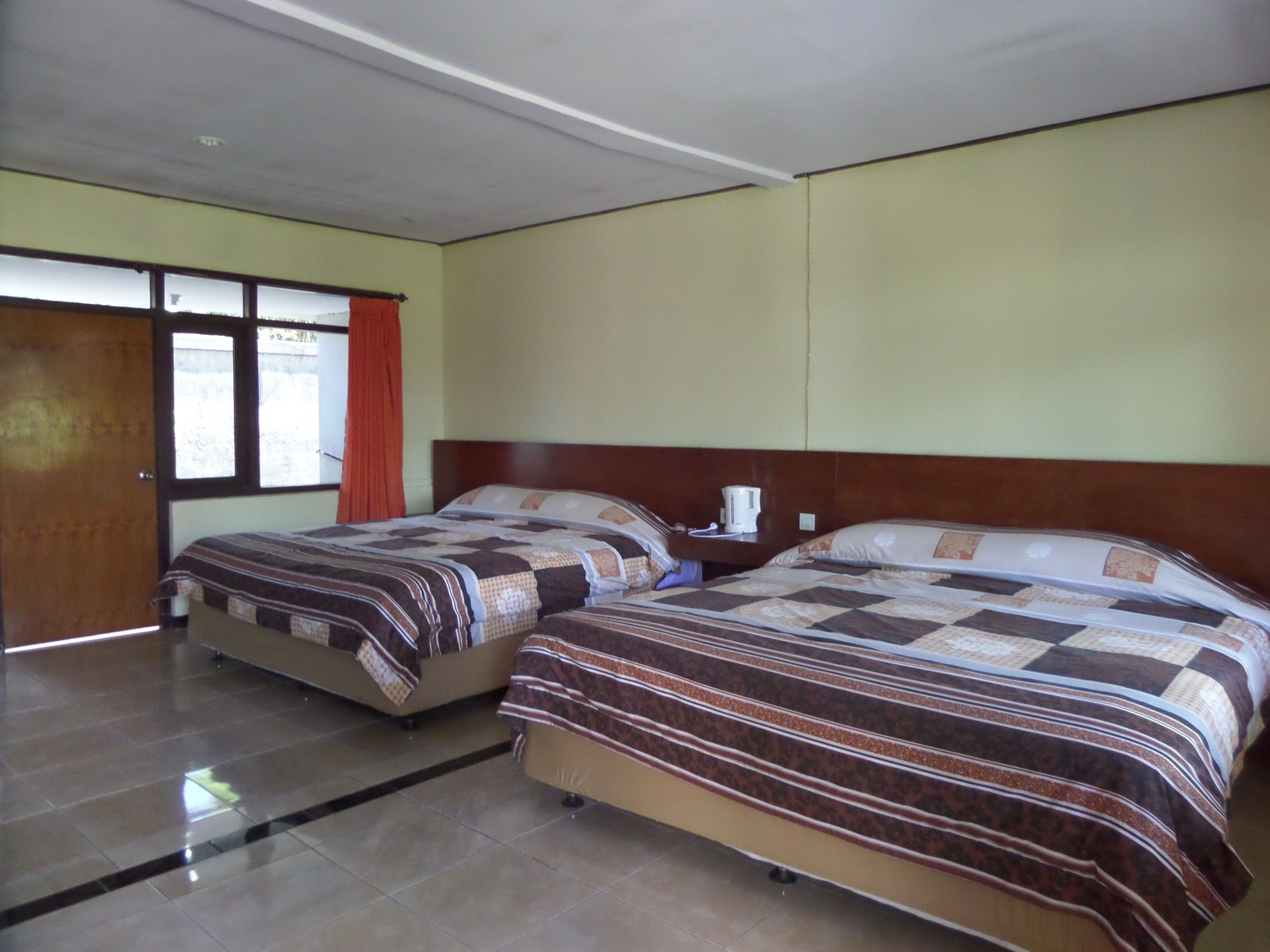 Two single beds with striped bedding in a room with a tiled floor and a wooden door.