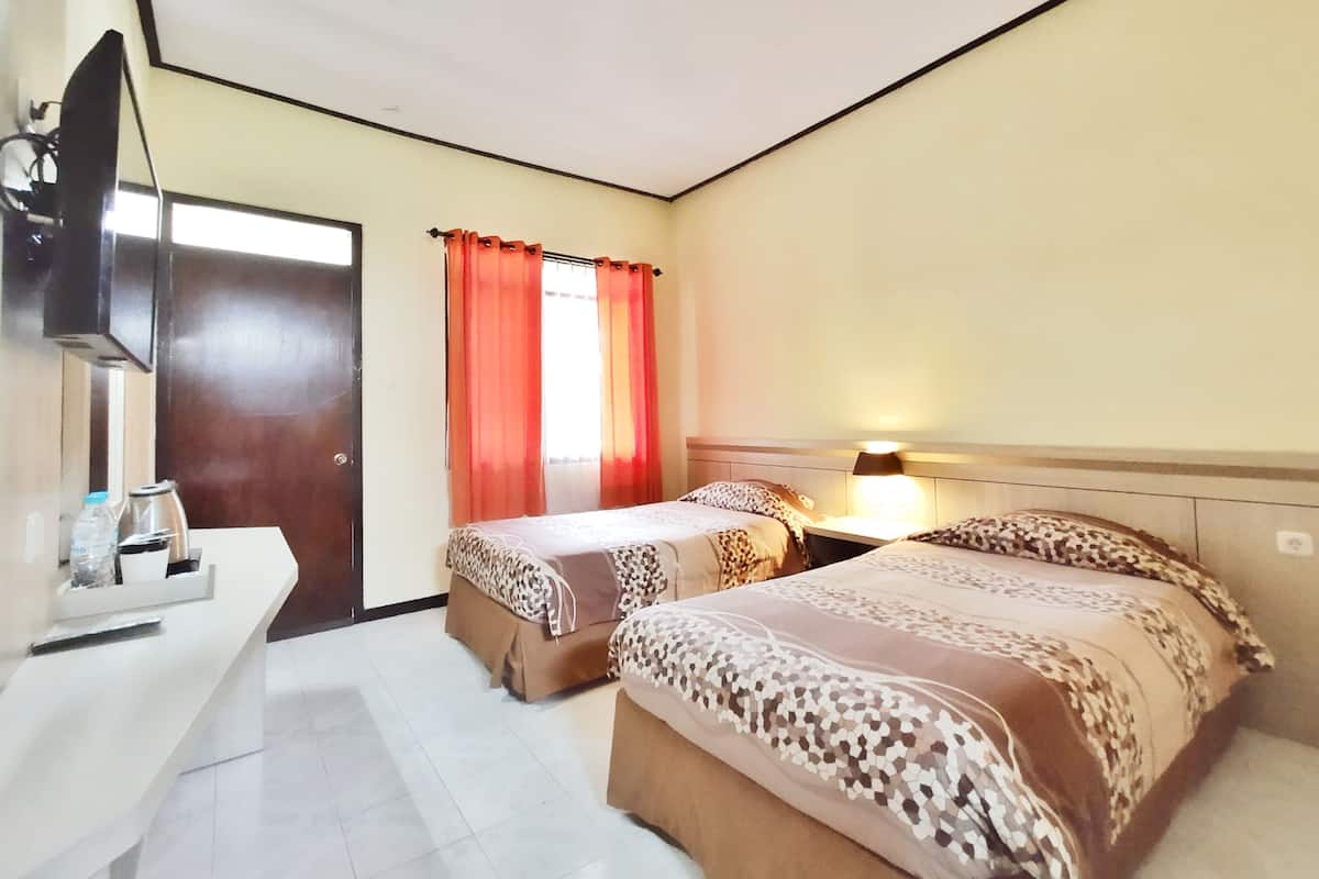 Quarto de hotel com duas camas, uma escrivaninha, televisão e janela com cortinas.