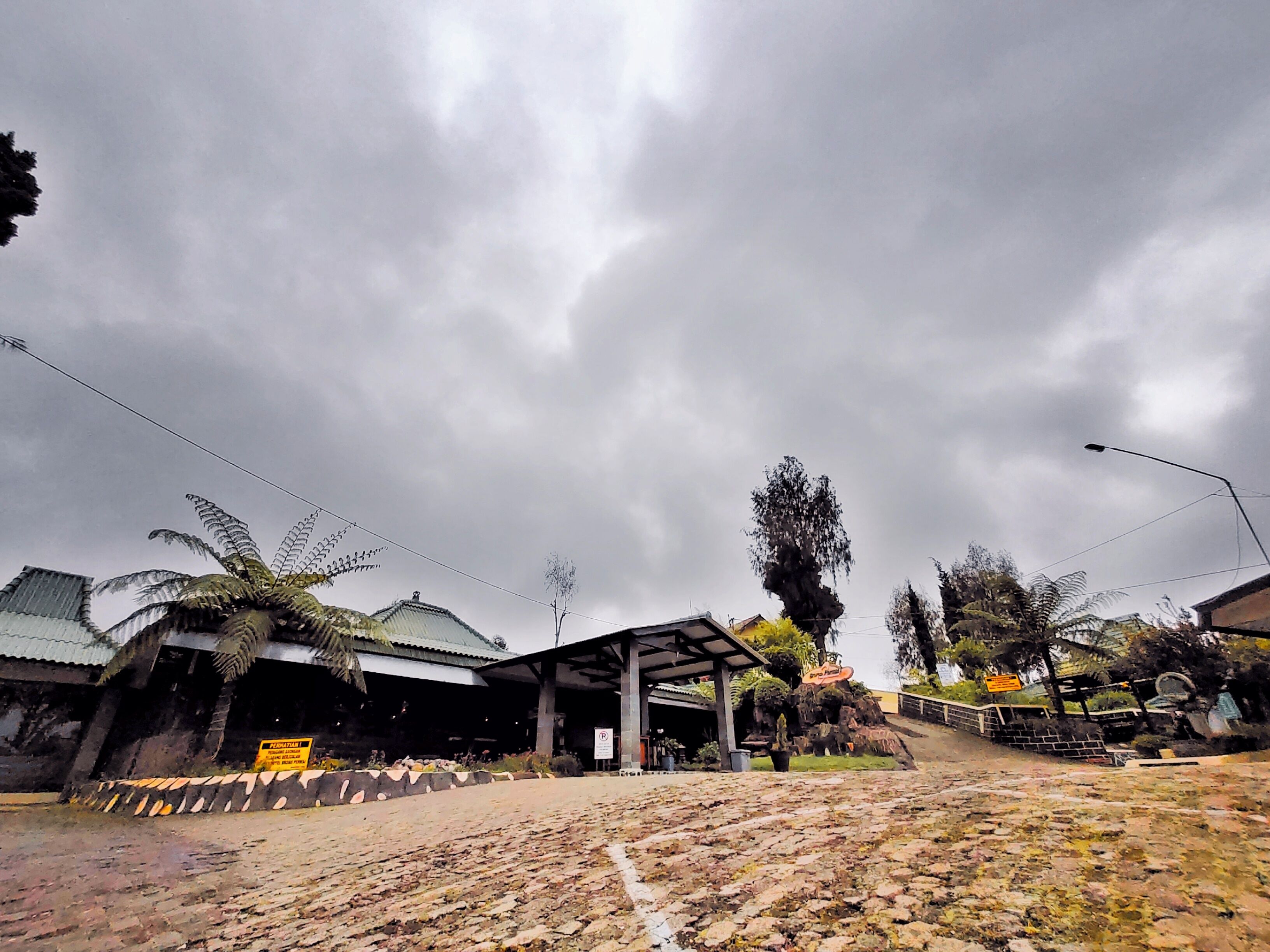 A building with a covered entrance, a sign indicating a parking area, and a paved area with a stone pattern.