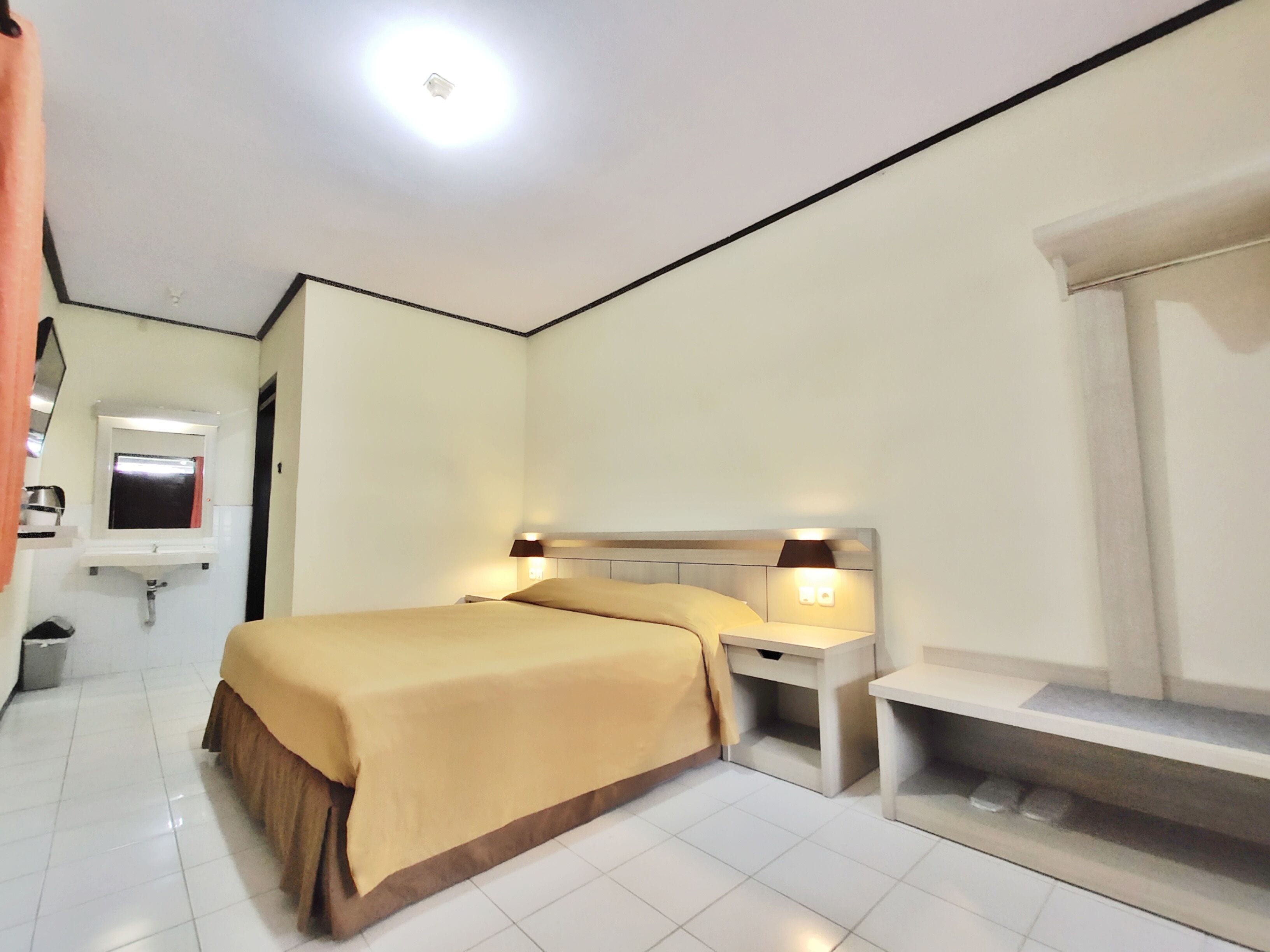 Une chambre d’hôtel avec un lit, des tables de chevet, un miroir, un lavabo et une fenêtre.