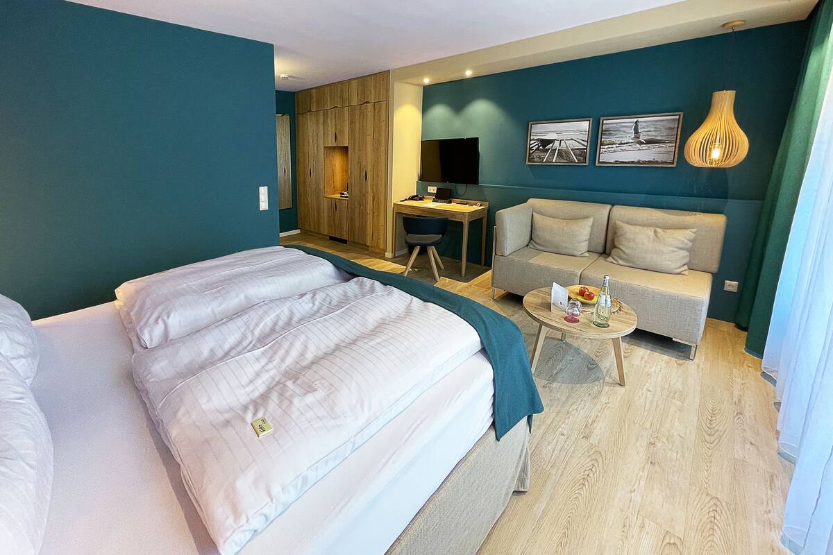 Habitación de hotel con una cama grande, un sofá, un escritorio y una mesita con una botella y vasos.