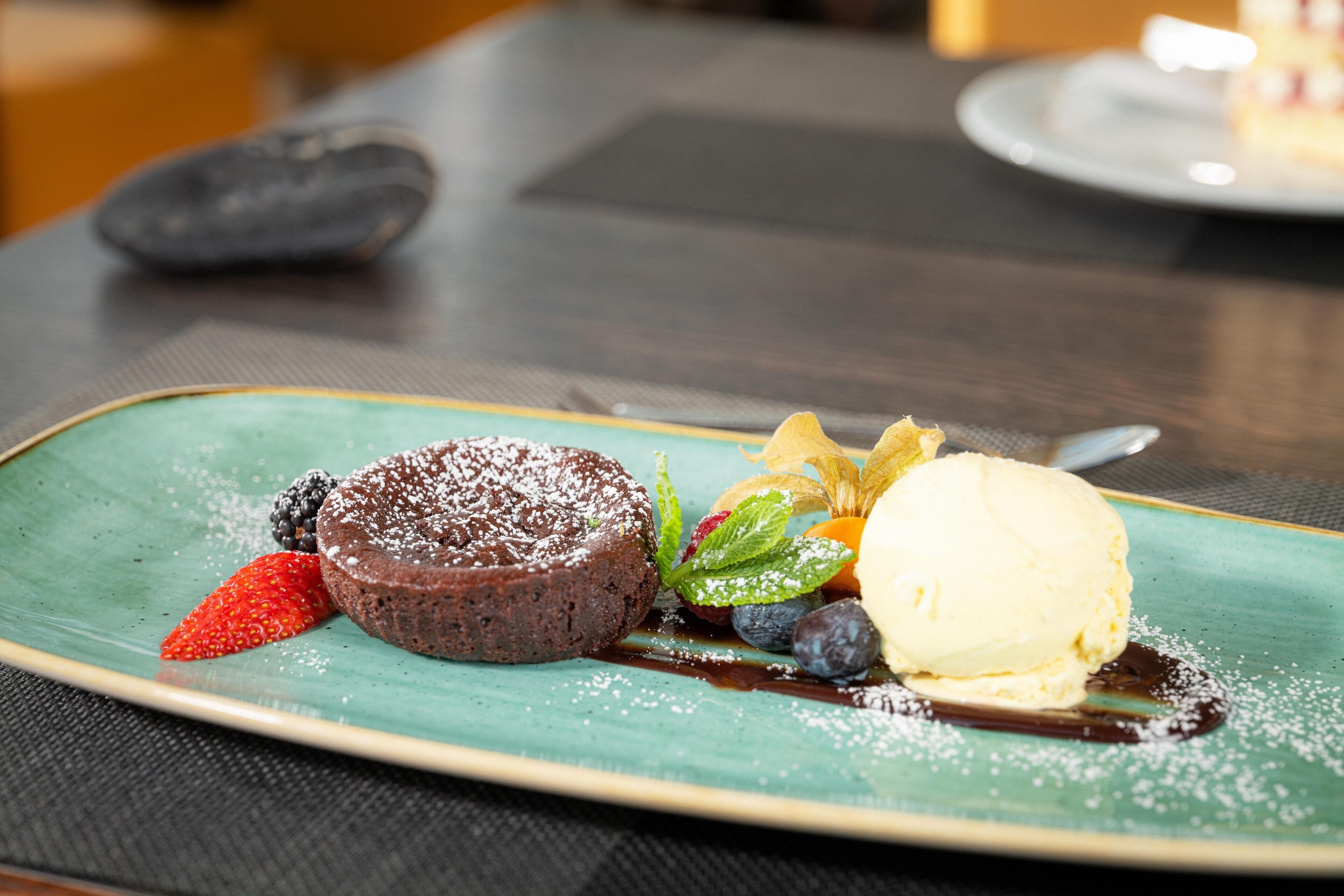 Ein Dessertteller mit Schokoladenkuchen mit flüssigem Kern, Eiscreme und Beeren auf einer grünen Untertasse.