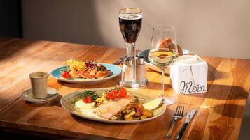 A wooden table with plates of food, glasses of wine, and a salt and pepper shaker.