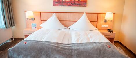 Habitación de hotel con una cama grande, dos lámparas de noche, un cuadro en la pared y una mesita de noche con un teléfono.