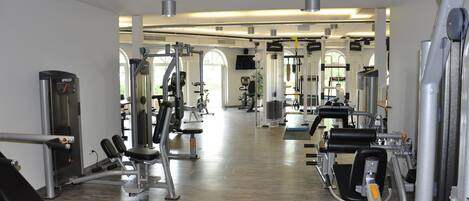 Un gimnasio con diferentes máquinas de ejercicio, un espejo grande y suelo de madera.