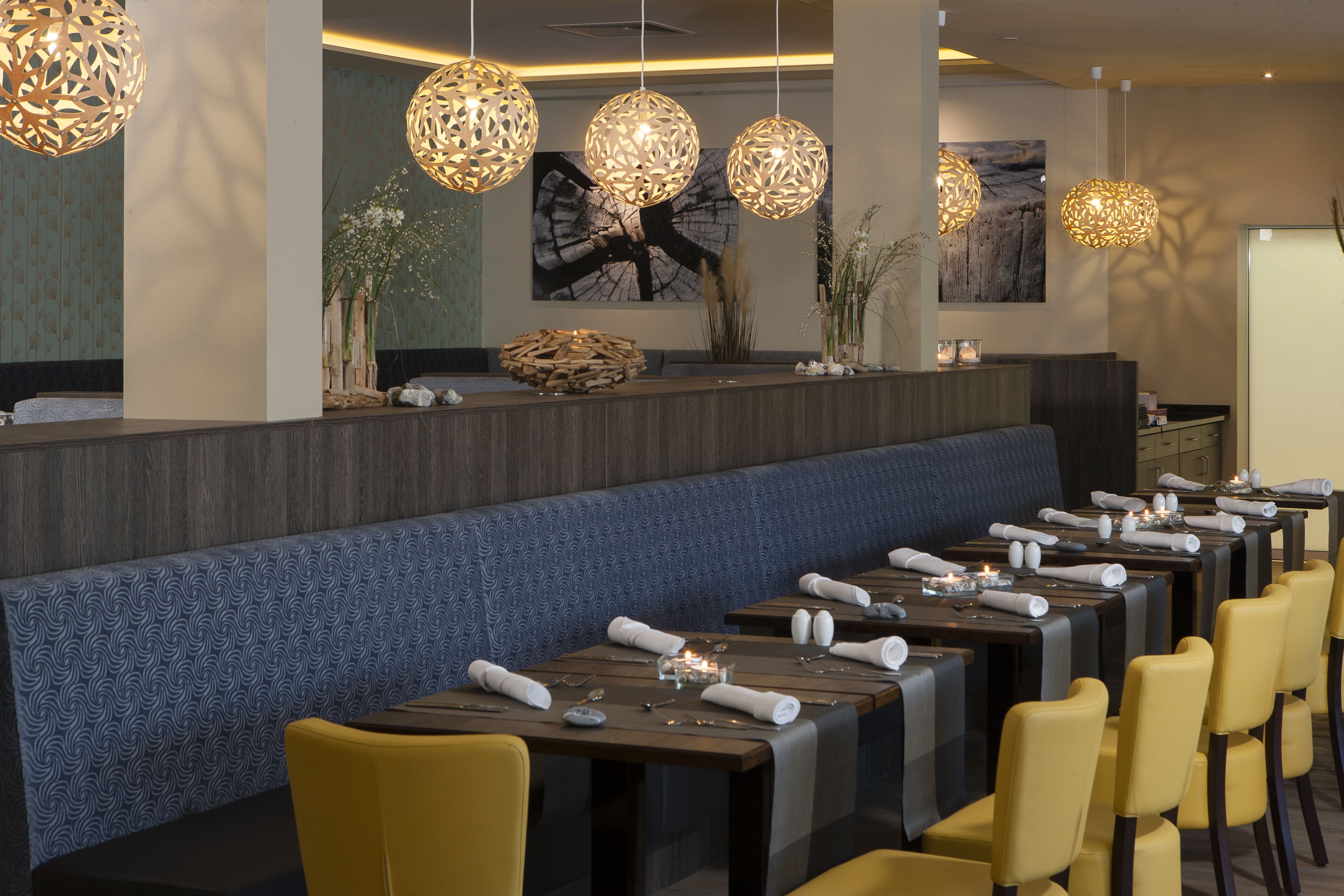A restaurant with a long counter, multiple tables, and yellow chairs.