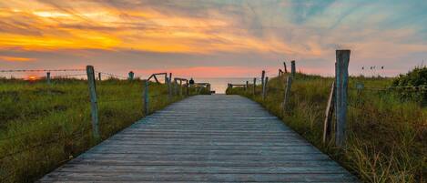 A wooden boardwalk leading to a beach with a sunset in the background.