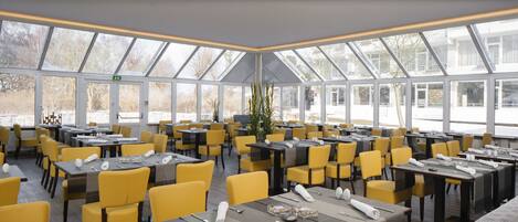 En rummelig restaurant med gule stole og borde, store vinduer og moderne indretning.