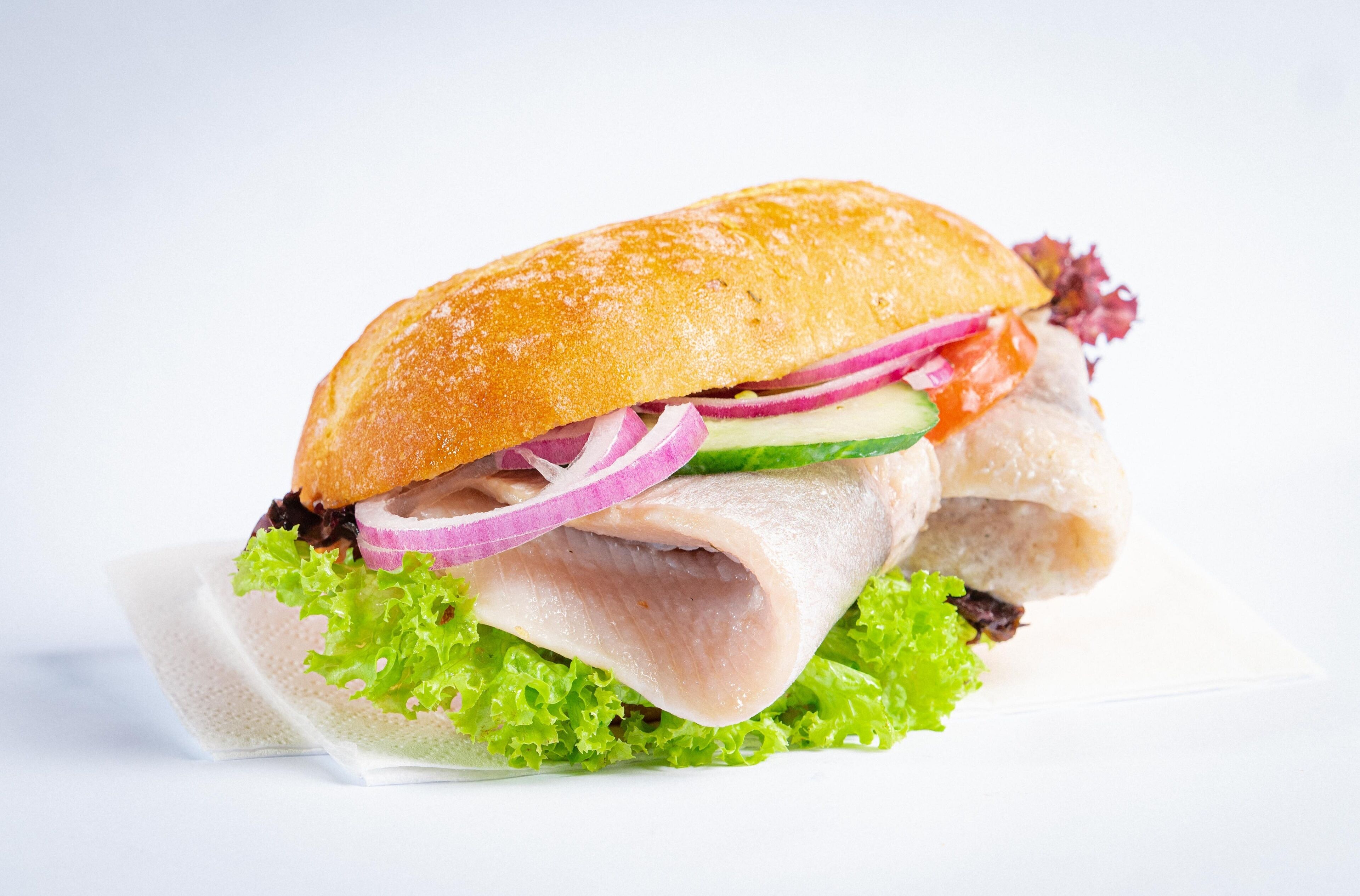Un sándwich de carne con lechuga, cebolla roja y pepino sobre un pan baguette.