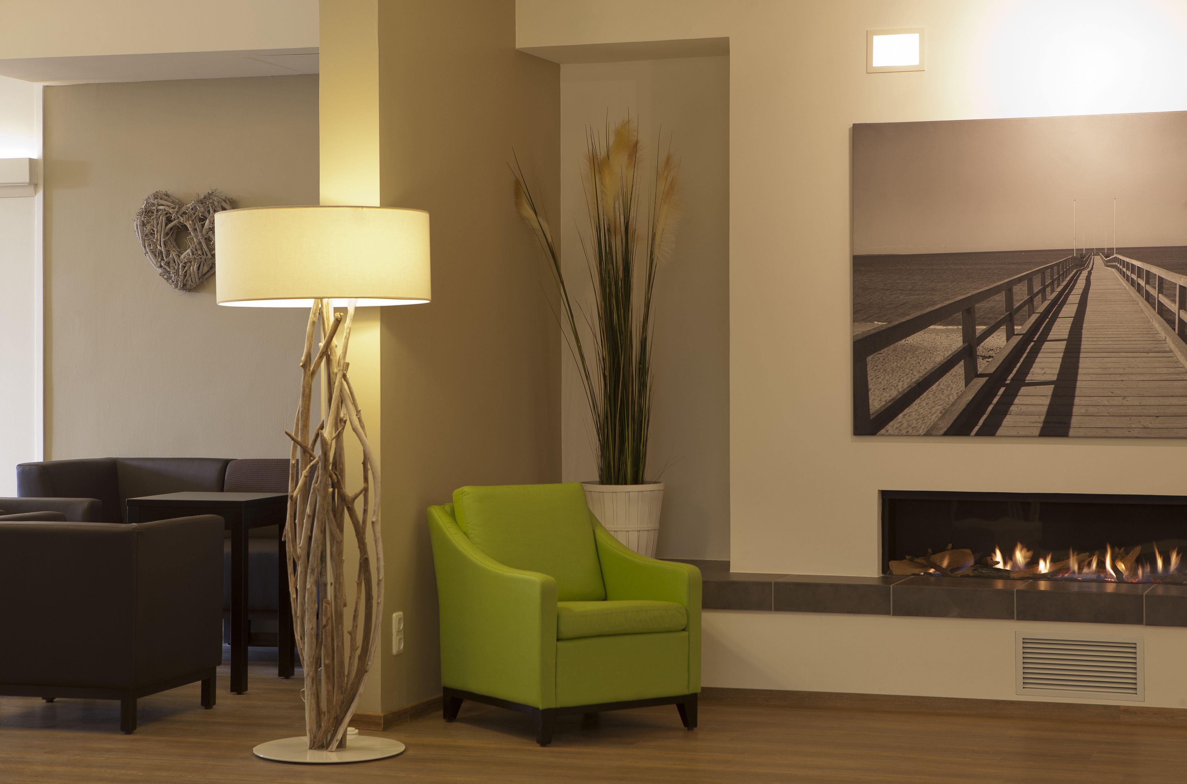 Ein modernes Wohnzimmer mit einem grünen Sessel, einer Stehlampe, einem Kamin und einem an der Wand hängenden Gemälde eines Piers.