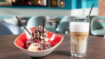Un tazón de postre con helado y trozos de chocolate, junto a un vaso de batido sobre una mesa de madera.
