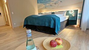 Habitación de hotel con una cama, una mesita de noche, una botella de agua y dos manzanas sobre una mesa.