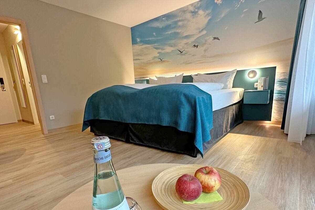Habitación de hotel con una cama, una mesita de noche, una botella de agua y dos manzanas sobre una mesa.