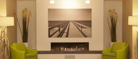 A modern living room with a fireplace, two green armchairs, and a large framed picture of a pier.