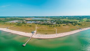Vista aérea de una zona costera con playa, muelle y área residencial con edificios y zonas verdes.