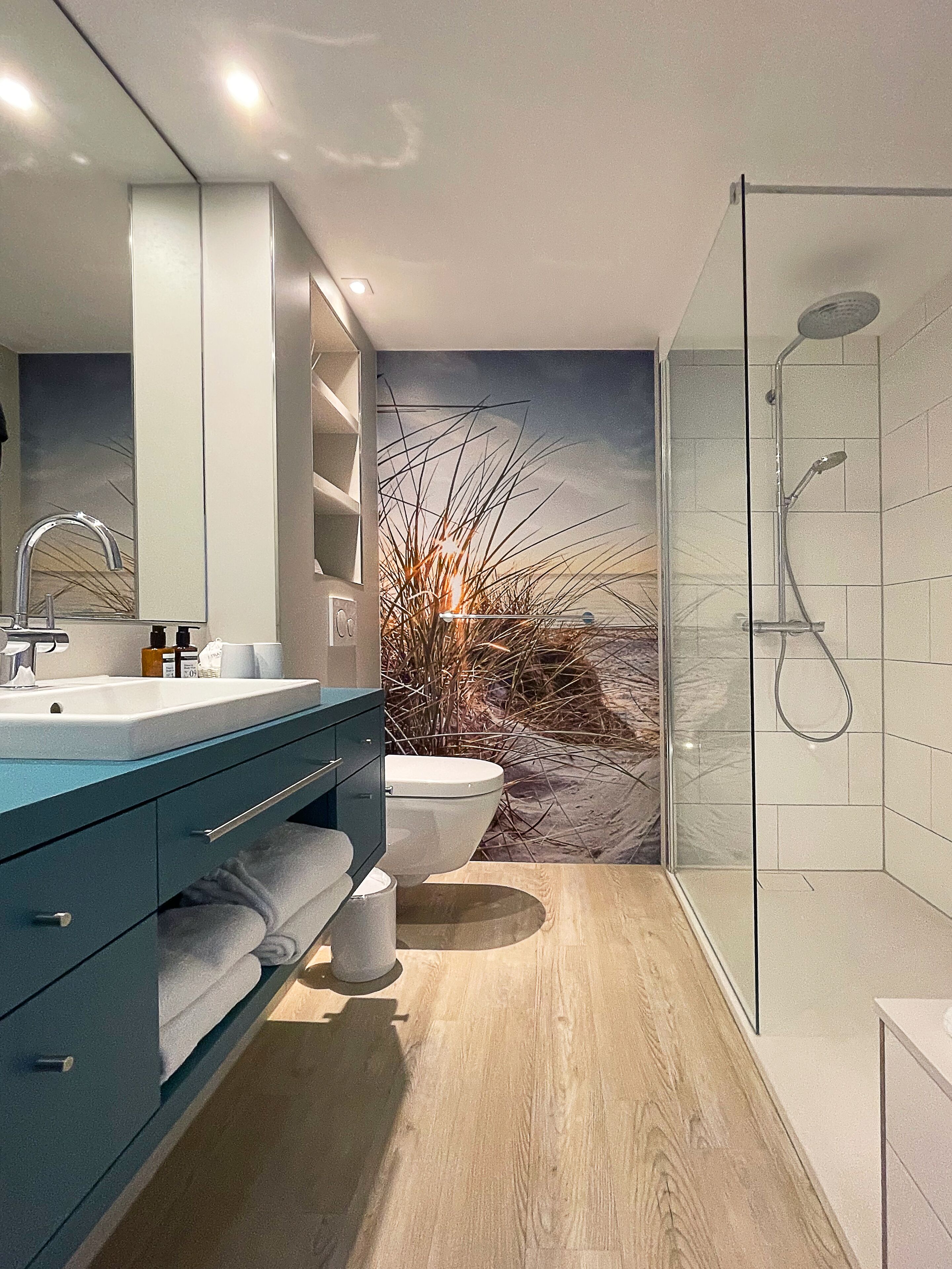 A modern bathroom with a large mirror, a sink, a toilet, and a glass shower enclosure.