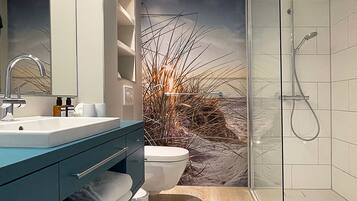 A modern bathroom with a large mirror, a sink, a toilet, and a glass shower enclosure.