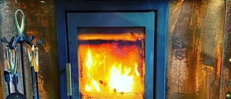 Una chimenea con fuego a la vista, una escoba y una pala a la izquierda.