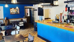 Un espace bar avec un comptoir bleu, des tables en bois et des lampes suspendues.