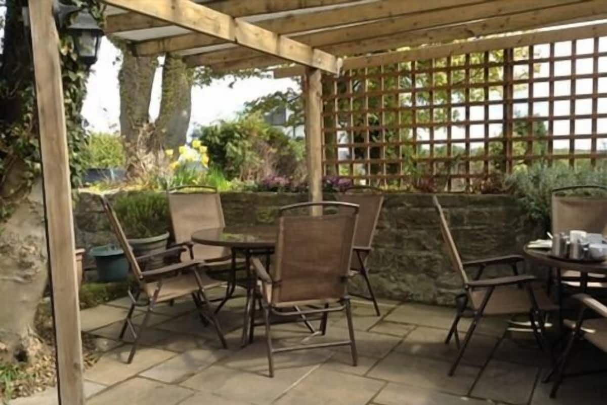 An outdoor patio with a wooden pergola, stone walls, and potted plants.