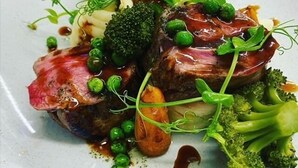 Une assiette de nourriture comprenant un steak, des brocolis, des petits pois et de la sauce.