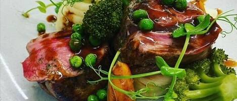 A plate of food with steak, broccoli, peas, and sauce.