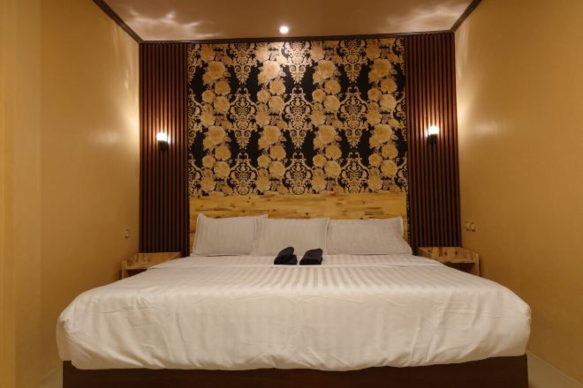 Una cama bien hecha con sábanas blancas, cabecera de madera y un diseño de papel tapiz estampado.